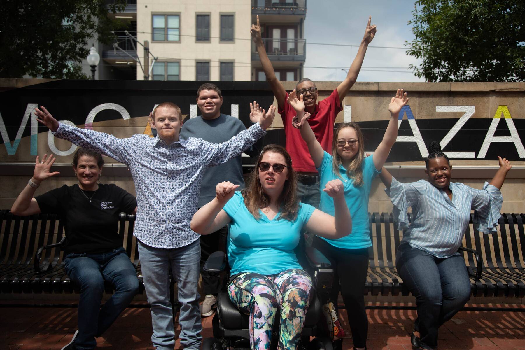 A group of friends cheer with arms raised in front of the McCall Plaza sign.