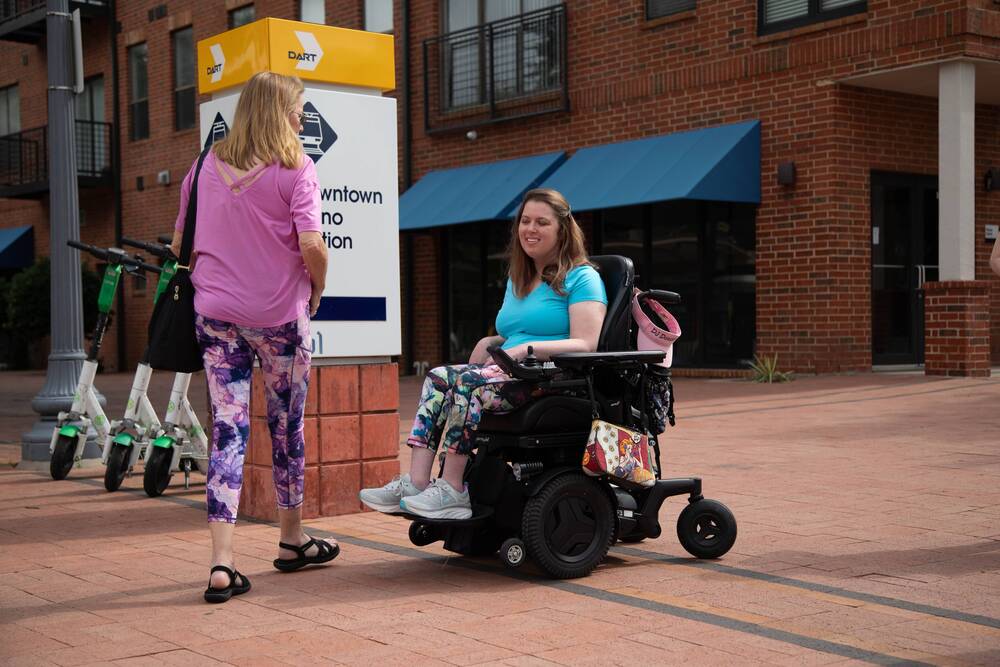 A woman using a power wheelchair waits outside the Downtown Plano station.
