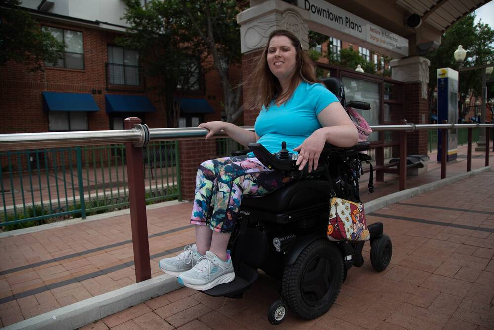 A woman in a power wheelchair smiles on a train platform.
